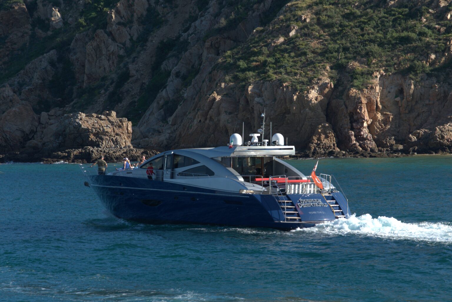 Dark blue sport yacht cruising past a rocky coastline